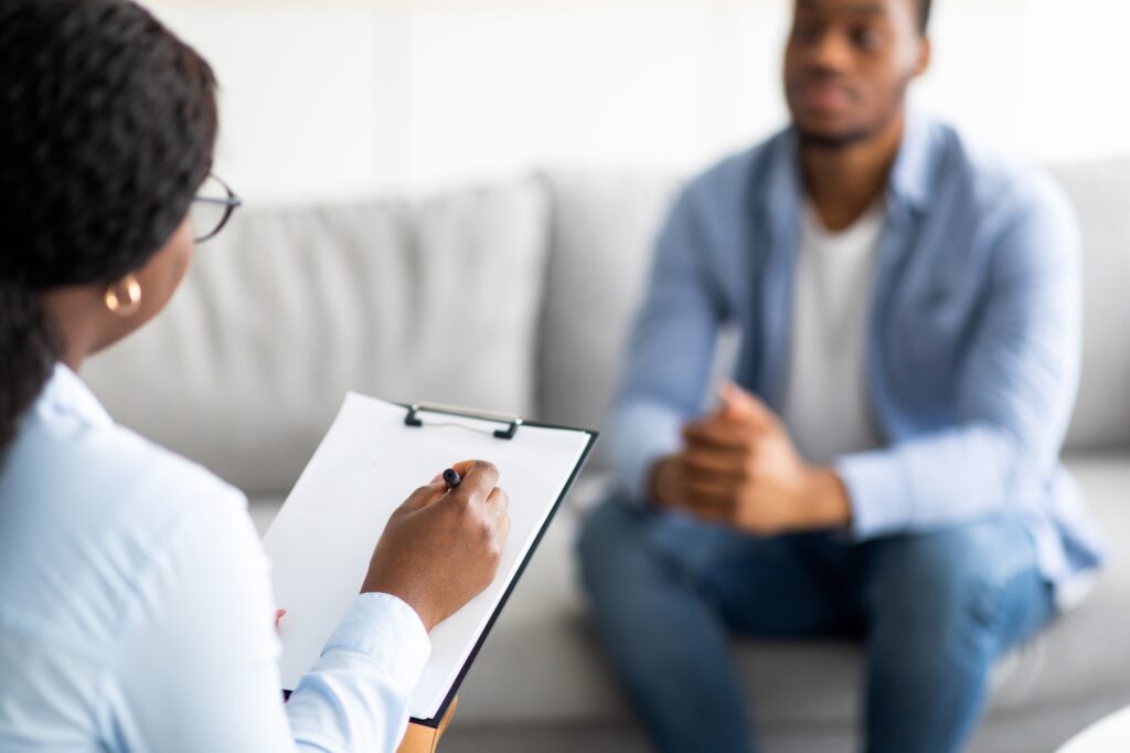 Young black guy with depression or PTSD having session with psychotherapist at clinic, selective